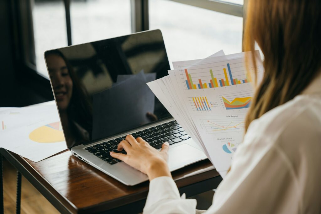 Businesswoman working and comparing forecasting and graphic documents paperwork with laptop